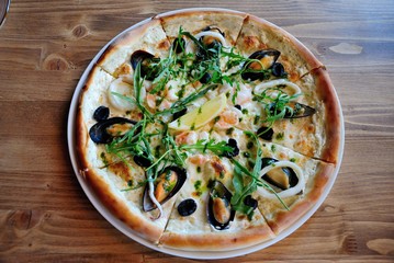 Seafood pizza with mussels, squid and shrimps, topped with olives, onion, herbs and lemon