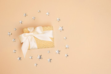 Traditional sparkling golden present box with a satin bow on pastel background decorated with shiny silver stars. Copy space.