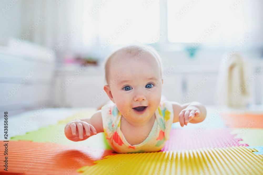 Wall mural baby girl lying on colorful play mat on the floor