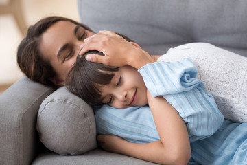 Loving mother caressing cute little daughter lying on sofa together, caring mom embracing kid relaxing enjoying nap, happy mum stroking hugging preschool girl cuddling resting on comfortable couch