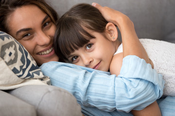 Loving tender mom embracing adorable little daughter relaxing on sofa, caring smiling mother...
