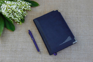 bouquet of white lilies of the valley with green leaves on a linen tablecloth on a Desk with a notebook and a pen top view