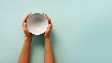 Female hand holding white empty bowl on blue background with copy space. Healthy eating, dieting...