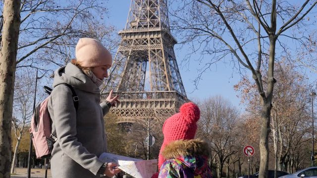 Mother with daughter child tourists watch paper city map near the Eiffel tower