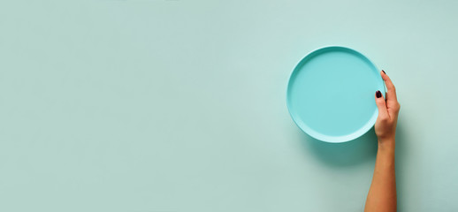 Female hand holding empty blue plate on pastel background with copy space. Healthy eating, dieting...