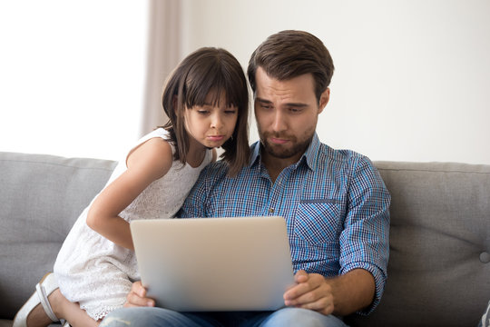 Cute empathic child girl and father make upset faces watching online cartoon together, kid daughter and dad feel pity compassion or sad by losing game application using laptop look at screen at home