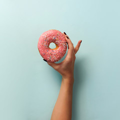 Female hand holding sweet donut over blue background. Top view, flat lay. Square crop. Weight lost,...