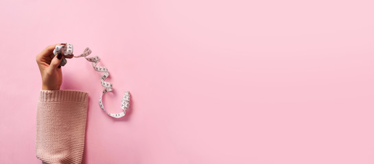 Female hands holding measuring tape over pink background. Top view, flat lay. Sweet, dessert, diet concept. Banner with copy space. Weight lost after holidays