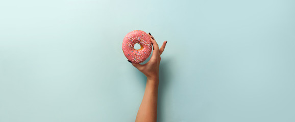 Female hand holding sweet donut over blue background. Top view, flat lay. Weight lost, sport,...