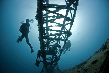 Scuba Divers on a ship wreck in clear blue water with sun in the background