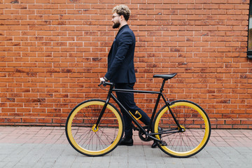 Fototapeta premium Businessman commuter with bicycle walking home from work in city agaist street brick wall