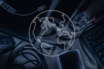 Items of information technology: cables, laptop, keyboard, smartphone, crimper. Contrasting light. In the foreground is a contour luminous image of the planet as a symbol of the globalization