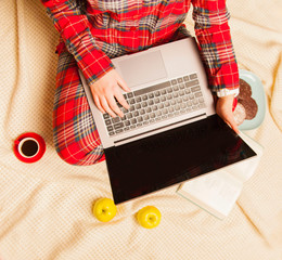 Girl in red pajamas with a Cup of coffee, laptop in the morning. On a white blanket.