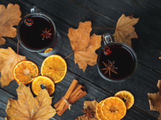Hot drink mulled wine on a wooden table with autumn leaves, cinnamon and citrus