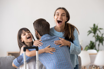 Excited wife and kid daughter hugging father arriving returning after long trip with suitcase,...