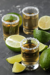 gold tequila in a glass shot glass with salt and lime close up on a black concrete background. bar. alcoholic beverages