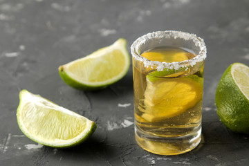 gold tequila in a glass shot glass with salt and lime close up on a black concrete background. bar....