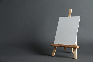 Wooden easel with blank canvas board on dark background, space for text. Children's painting