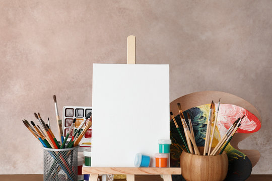 Wooden easel with blank canvas board and painting tools for children on color background