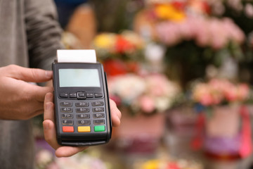 Man holding payment terminal in floral shop, closeup. Space for text