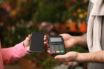 Woman using terminal for contactless payment with smartphone in floral shop, closeup. Space for text