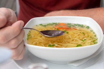 Delicious Vegetable soup with noodles in white bowl, stainless steel spoon in hand, ready to eat