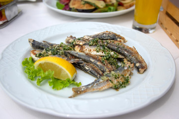 Group of grilled anchovies on white plate with yellow fresh lemon and green salad, delicious sea food