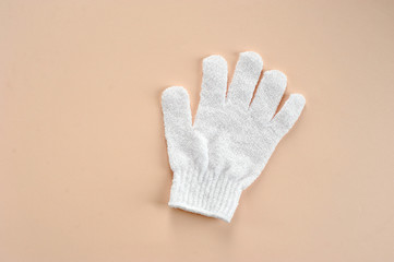 White exfoliating glove. Polyacrylate glove for use in the shower. Glove tones, cleanses, massages the skin. Beige background Close-up. View from above.