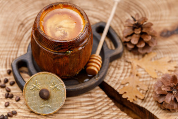 Open barrel with honey on a wooden saw with a spoon for honey and pine cones.