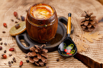 An open keg of honey and a painted wooden Russian spoon on a wooden sawn with pine cones.