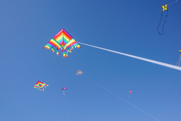 angle view of a colorful kite flying with waving red bow in a deep blue sky with the light of the sun