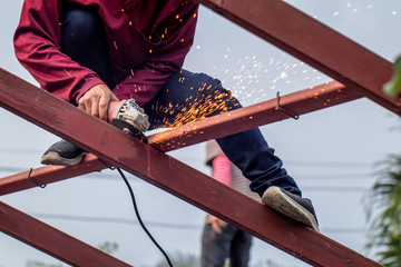 The man wearing brown shirt is cutting or sawing the metal on the roof construction by the metal saw on the top of the house in the sunny day. 