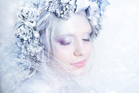 Portrait of young beautiful woman with winter style head decoration, silver body art and fairytale makeup on frosty background