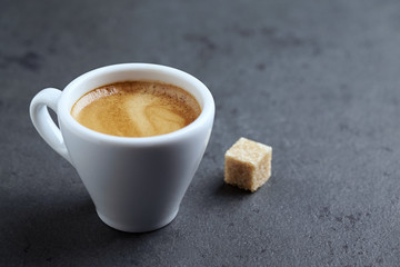 Cup of coffee and a brown sugar cube on black stone background. Close up. Copy space
