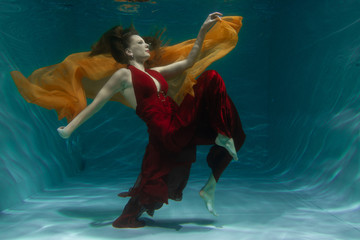 beautiful free diver woman swimming in long red evening dress under water alone in the deep