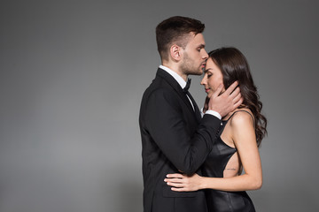handsome man kissing forehead of beautiful girlfriend isolated on grey