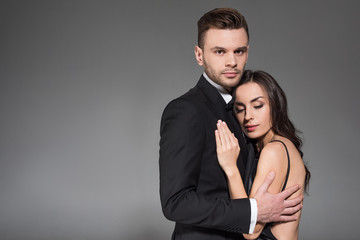 beautiful elegant couple in black clothes hugging together isolated on grey