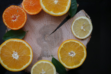 Oranges and tangerines sliced on a wooden saw cut, on a black background