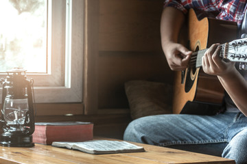 close up young male playing guitar and sing a song from christian hymn book on wooden table.