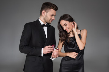 handsome boyfriend holding proposal ring in box for beautiful girlfriend, isolated on grey