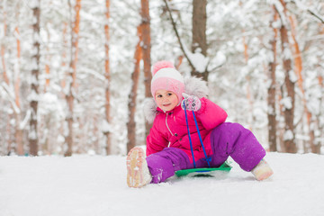 little girl riding down a hill in a winter pine forest