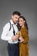 young smiling couple hugging and holding champagne glasses isolated on grey