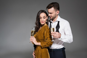 young happy couple hugging and holding champagne glasses isolated on grey