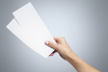 Female hand holding two blank sheets of paper (tickets, flyers, invitations, coupons, banknotes, etc.) on gray background