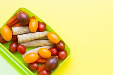 School lunch box. Candies, baby corns, carrot and tomatoes in green plastic container