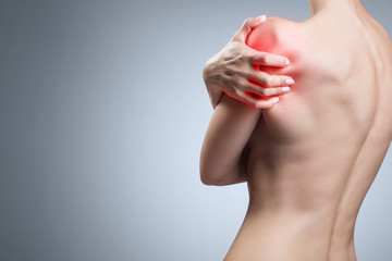 Young woman suffering from pain in her shoulder on gray background