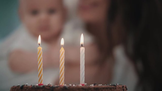 Mother blowing three candles at baby birthday cake. Baby birthday party concept
