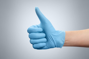 Hand in a blue rubber glove with thumb up on gray background