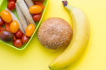 School lunch box. Bread, a banana, candies, baby corns, carrot and tomatoes in green plastic container