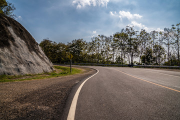 Road in the mountains. Empty asphalt road through the green Thailand hills and clouds on blue sky in summer day